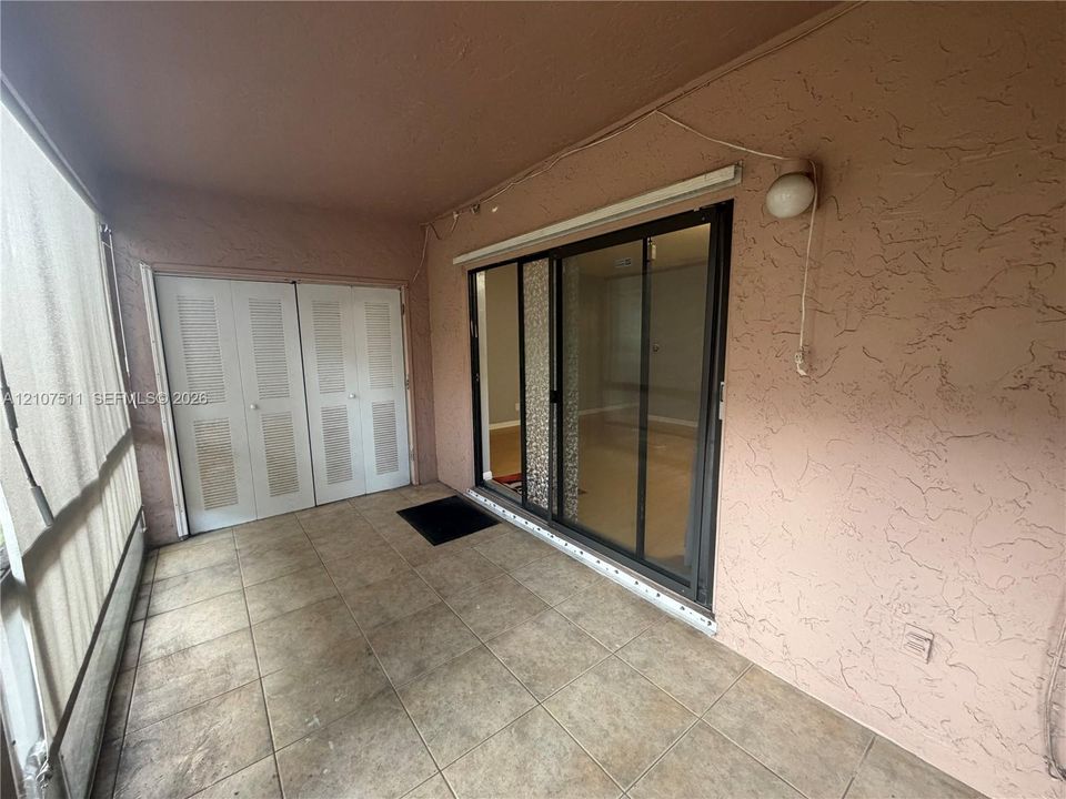 Covered patio featuring ceramic tile flooring, sliding glass doors, double louvered-panel closet doors, and textured stucco walls