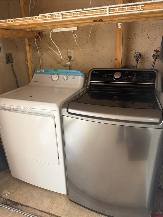 Laundry space featuring a stainless steel top-load washer, a high-capacity dryer, and integrated open wood shelving