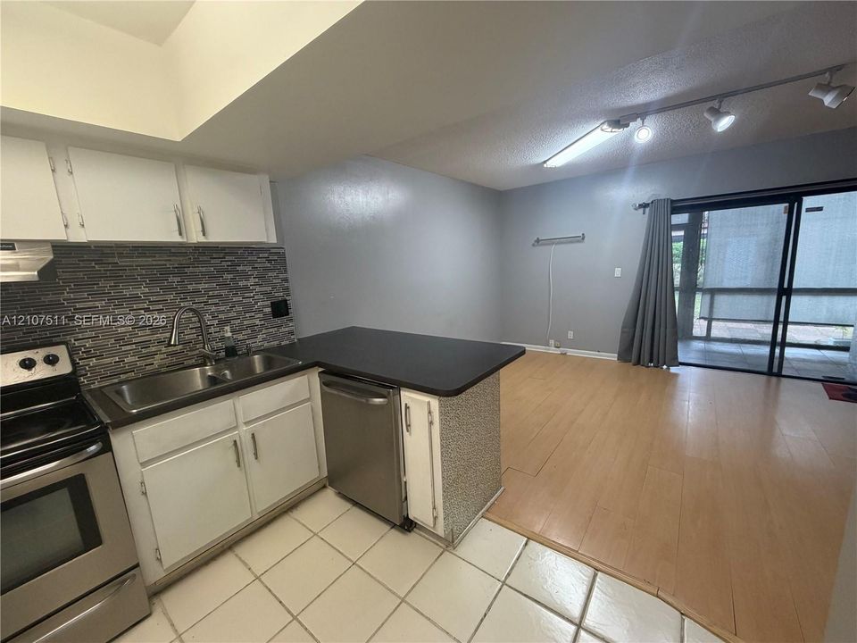 Kitchen featuring stainless steel appliances, multi-toned decorative tile backsplash, wood-finish flooring, and sliding glass doors