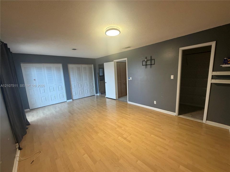 Room featuring wood-finish flooring, two sets of white louvered closet doors, and interior access to a secondary space