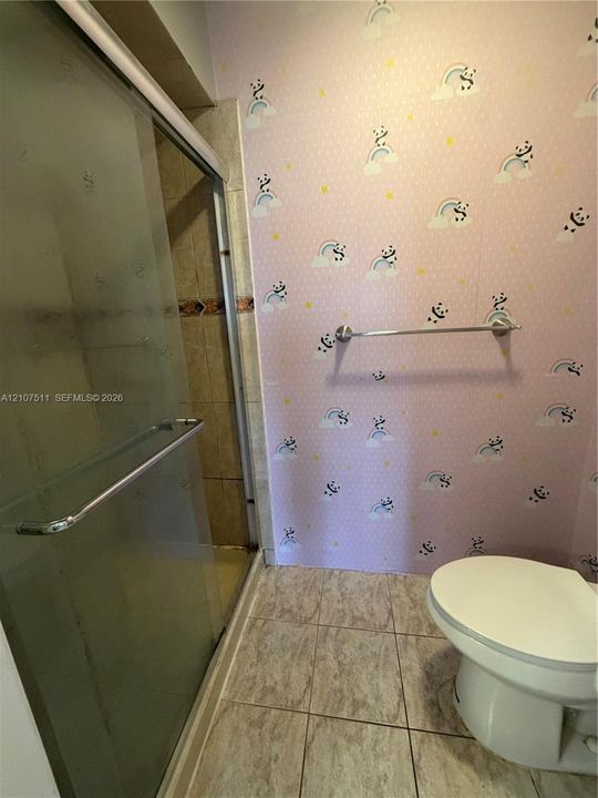 Shower enclosure with sliding glass doors, metal hardware, and tiled surround, featuring ceramic floor tile and a wall-mounted metal towel bar