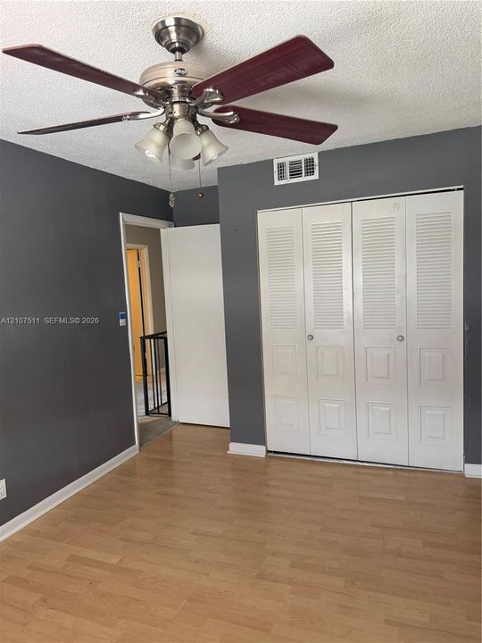 Wood-finish flooring, neutral-toned walls, ceiling fan with integrated lighting, and white louvered-panel closet doors