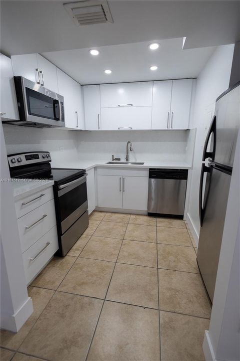 Kitchen featuring white cabinetry with brushed-metal pulls, stone-finish countertops, stainless steel appliances, and tile flooring