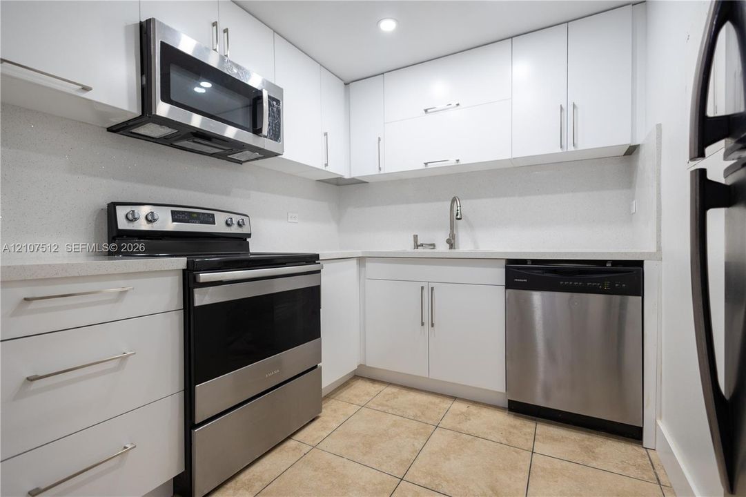 Kitchen featuring white flat-panel cabinetry, stainless steel appliances, solid surface countertops, a gooseneck faucet, and tiled flooring