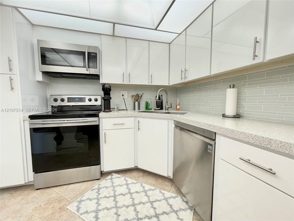 Kitchen featuring white cabinetry with metallic hardware, stone-composite countertops, stainless steel appliances, and a glass-tile backsplash