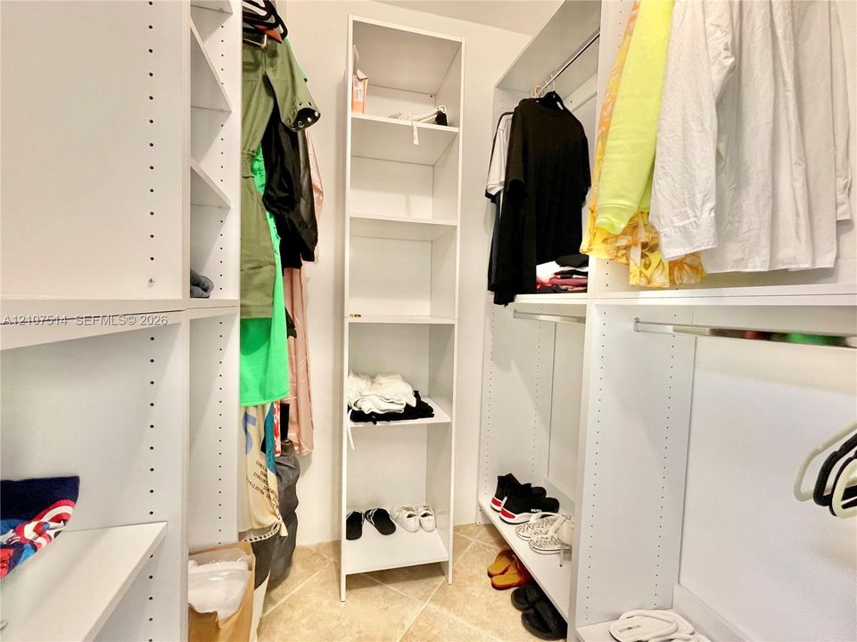Custom walk-in closet featuring white built-in shelving, adjustable storage racks, metal hanging rods, and tile flooring