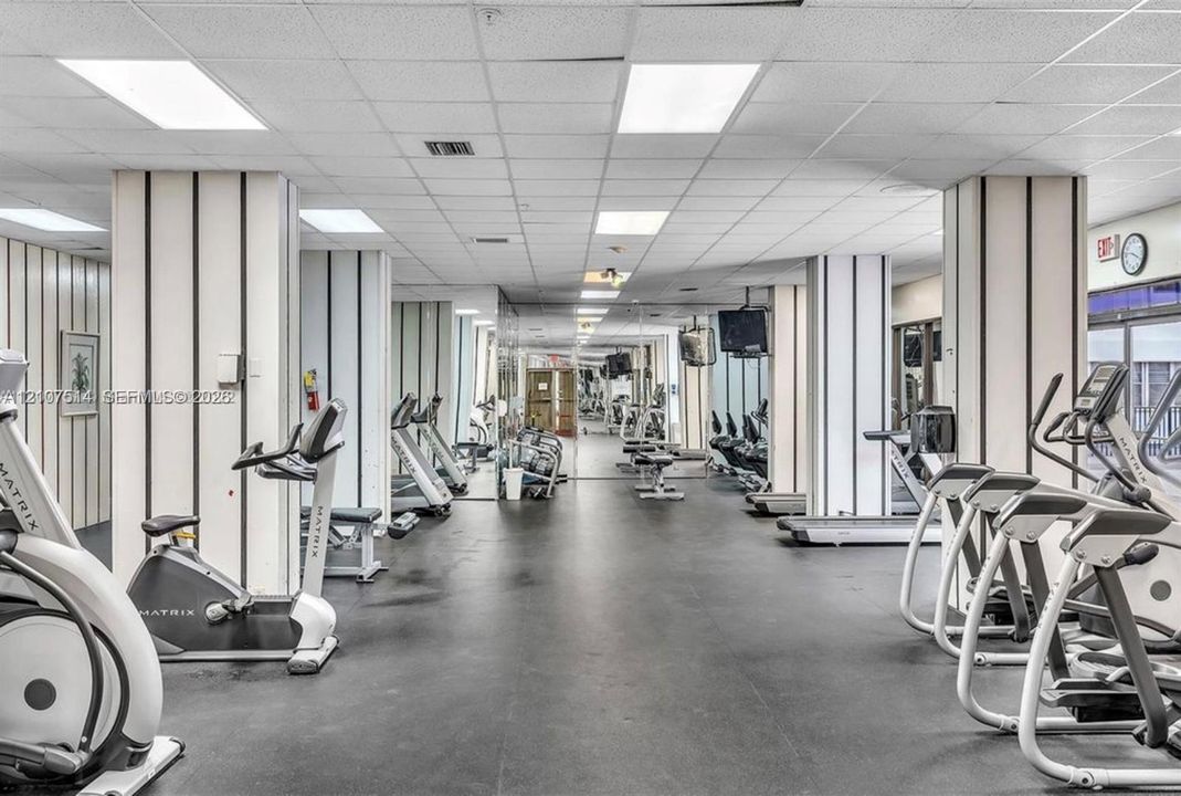 Fitness room featuring rubberized flooring, drop ceiling with recessed panel lighting, mirrored wall accents, and vertical pinstripe wall detailing