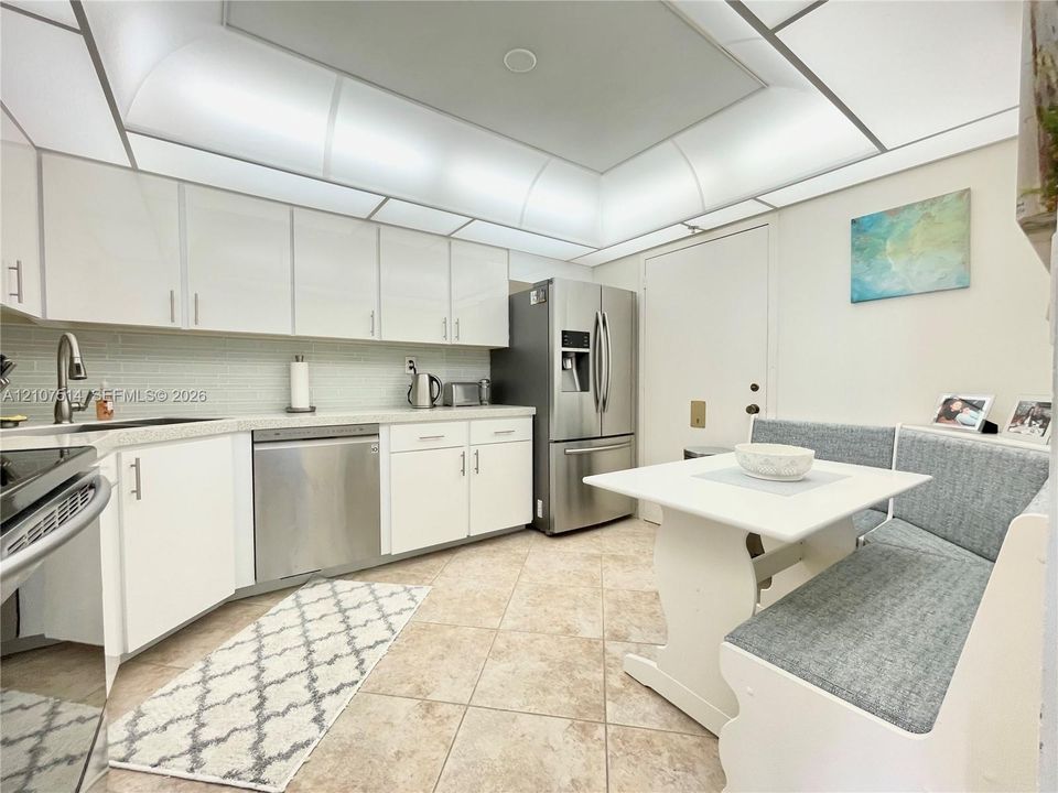 Kitchen featuring white cabinetry, stainless steel appliances, light-toned stone-finish countertops, tiled backsplash, and recessed cove lighting