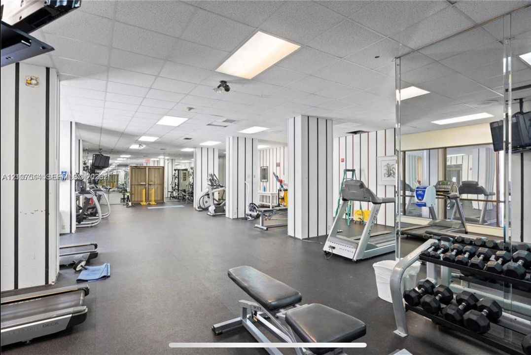 Fitness facility featuring rubberized flooring, mirrored walls, drop ceiling panels, and structural columns with vertical accent detailing
