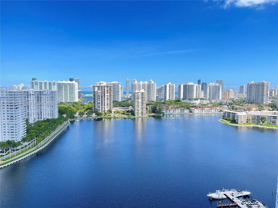 Expansive water frontage featuring a deep-water canal, boat docking structure, urban skyline backdrop, and dense perimeter landscaping
