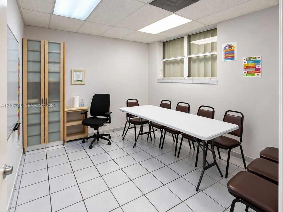 Room featuring light-colored tile flooring, drop ceiling with integrated rectangular lighting, tall built-in storage cabinet with frosted glass panels, and an elevated window