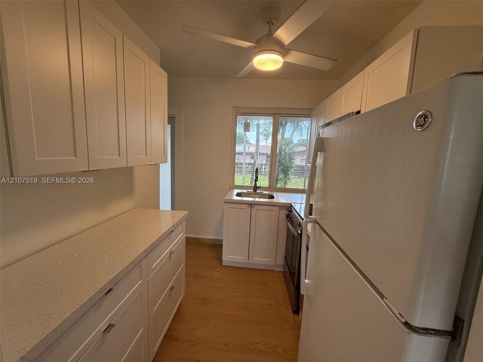 Kitchen featuring white Shaker-style cabinetry, light-toned speckled countertops, wood-finish flooring, a stainless steel sink, and a ceiling-mounted light fixture with integrated fan