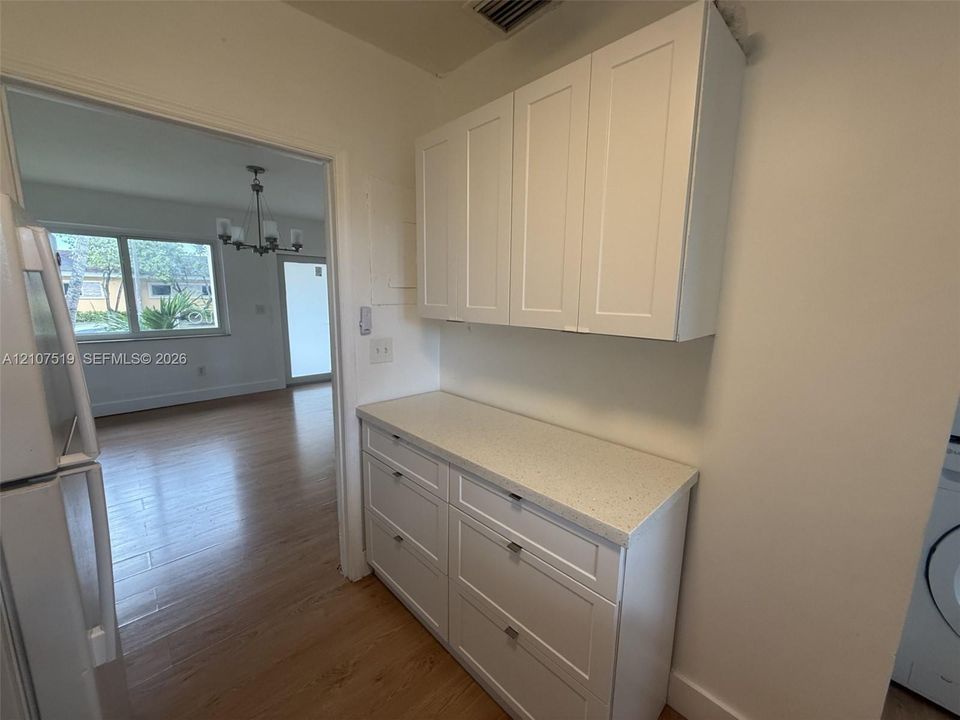 White shaker-style cabinetry with matte hardware, stone-composite countertop, and wood-finish flooring