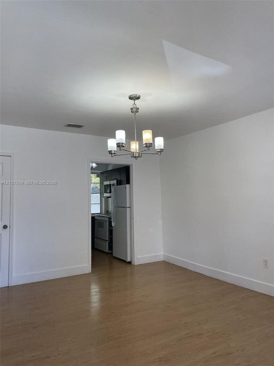 Neutral interior space featuring wood-finish flooring, a five-arm chandelier with frosted glass shades, and white wall finishes