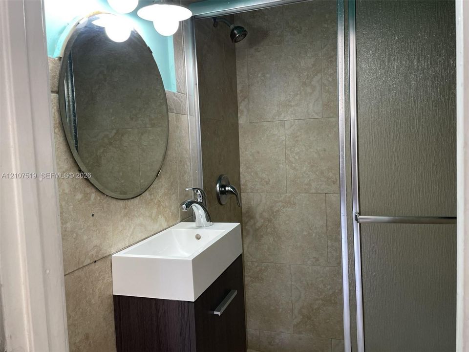 Bathroom featuring a floating vanity with a rectangular sink, stone-finish wall tile, an oval mirror, and a shower enclosure with a glass door