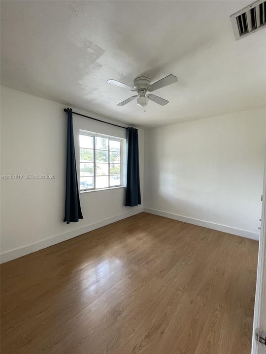 Room featuring wood-finish flooring, a multi-pane window, and a ceiling-mounted light fixture with fan