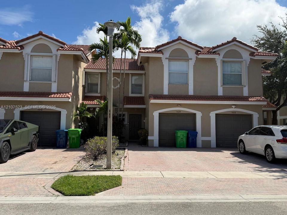Two-story exterior featuring a tile roof, stucco facade with decorative trim, and multi-car garage access with paver driveways
