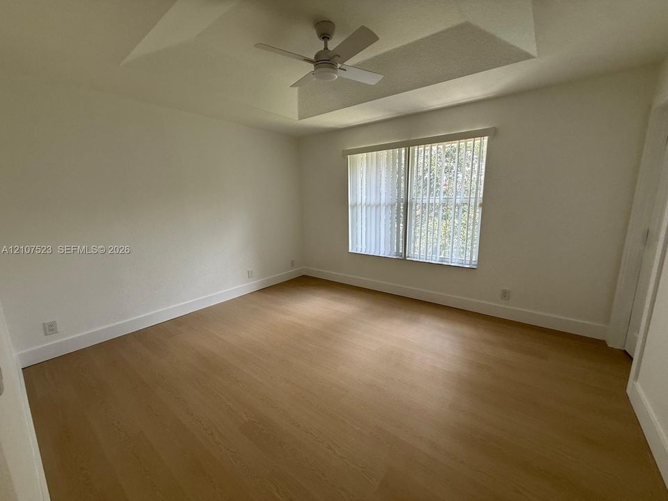 Room featuring wood-finish flooring, a tray ceiling, and a ceiling fan