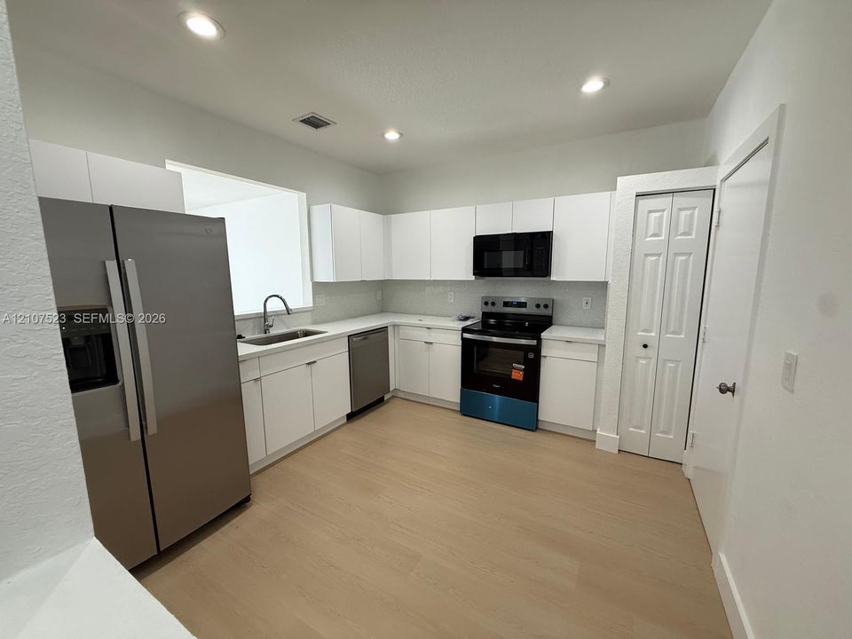 Kitchen featuring white flat-panel cabinetry, stainless steel appliances, wood-finish flooring, recessed lighting, and a neutral-toned backsplash
