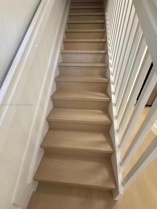 Staircase featuring light wood-finish treads, crisp white paneled wall detailing, and a minimalist white vertical spindle railing