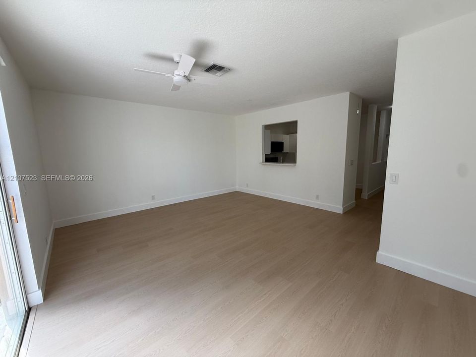 Open-concept interior featuring light wood-finish flooring, white walls, a ceiling-mounted fan, and a pass-through opening