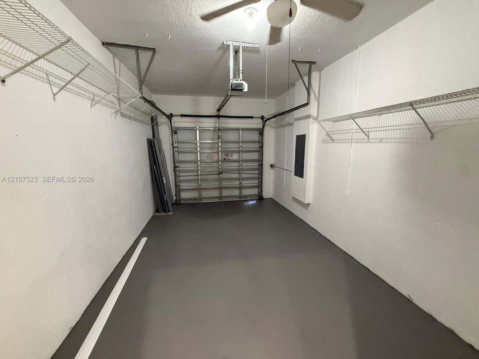 Finished garage featuring a smooth floor surface, white walls, overhead ceiling fan, and wall-mounted wire shelving
