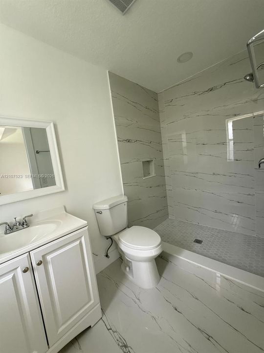 Bathroom featuring a walk-in shower with large-format tile surround, integrated shower niche, penny-round tile flooring, and a white vanity with an integrated sink and chrome faucet