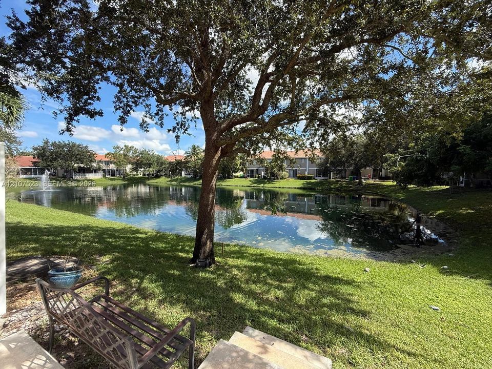 Waterfront lot featuring a natural pond, decorative fountain, mature shade trees, and manicured grass grounds