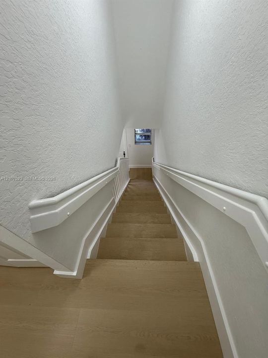 Staircase featuring wood-finish treads, smooth white wall finishes, and custom-fitted white handrails