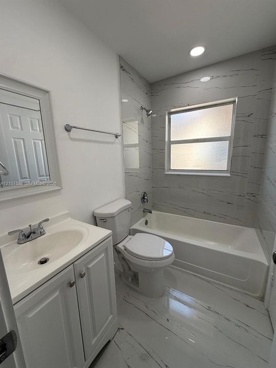 Bathroom featuring a vanity with integrated sink, large-format tile flooring, and a shower-tub combination surrounded by floor-to-ceiling tile with a decorative pattern