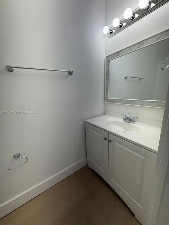 White vanity featuring an integrated sink, brushed metal hardware, wood-finish flooring, a framed mirror, and a multi-bulb vanity light fixture