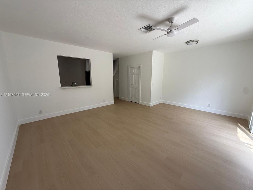 Neutral interior space featuring wood-finish flooring, a ceiling fan, a flush-mount light fixture, and a pass-through wall opening