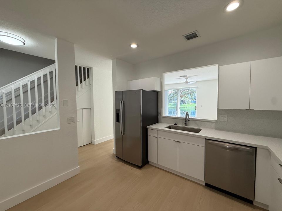 Kitchen featuring flat-panel white cabinetry, quartz countertops, stainless steel appliances, and wood-finish flooring, with a staircase featuring a white-railed balustrade