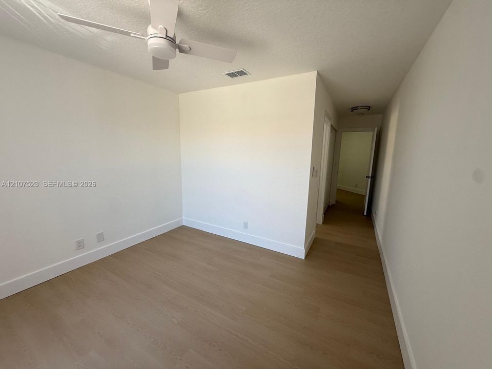 Neutral-toned interior space featuring wood-finish flooring, white walls, and a ceiling-mounted fan with integrated light