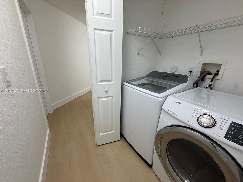 Laundry area featuring wood-finish flooring, bi-fold closet door, and built-in wire shelving