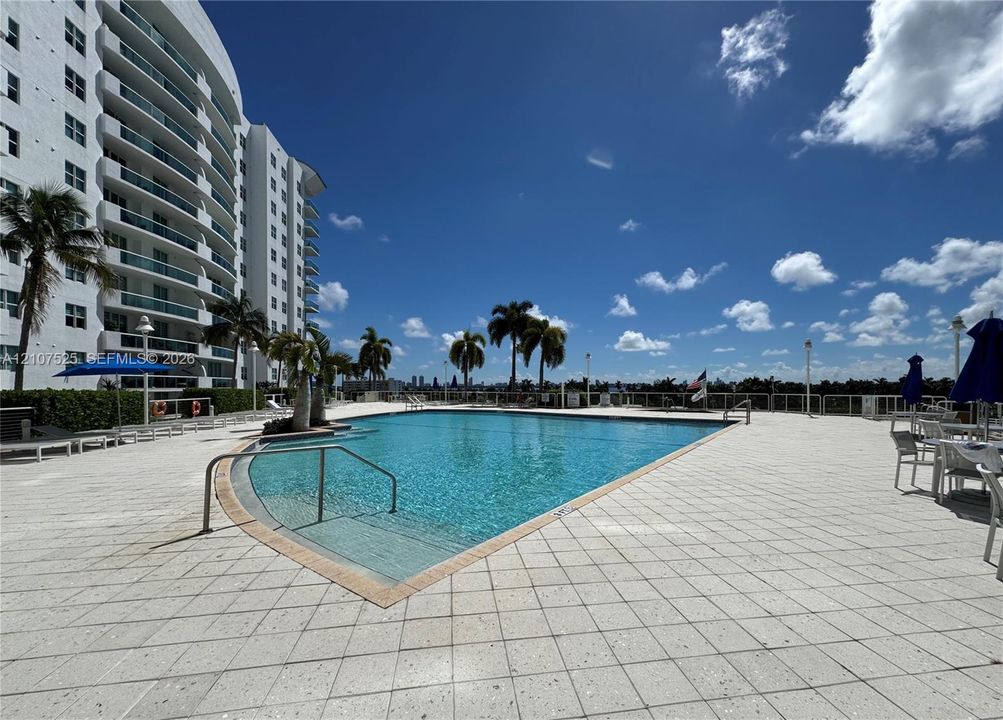 Swimming pool featuring a tiled deck, integrated steps, and metallic railings, surrounded by mature palm trees