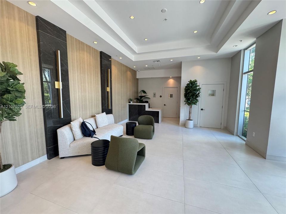 Lobby featuring a coffered ceiling with recessed lighting, large-format tile flooring, wood-finish wall paneling, and black stone accent pillars with integrated vertical lighting fixtures