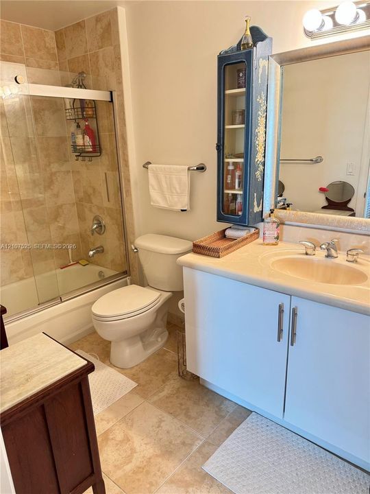Bathroom featuring a vanity with a solid surface countertop and integrated basin, bathtub-shower combination with glass sliding doors, stone-tile surround, and stone-finish flooring