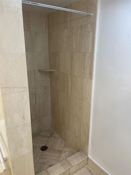 Walk-in shower featuring floor-to-ceiling stone-tile surround, neutral-toned finish, built-in corner shelving, and a tiled shower basin