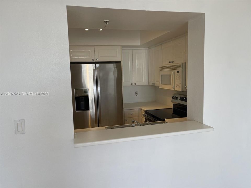 Kitchen featuring white cabinetry, stainless steel refrigerator, over-the-range microwave, solid-surface countertops, and a pass-through breakfast bar