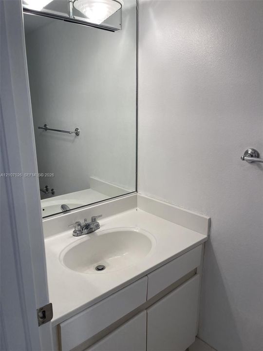 Vanity with integrated sink, solid surface countertop, chrome dual-handle faucet, large wall-mounted mirror, and attached metal hardware