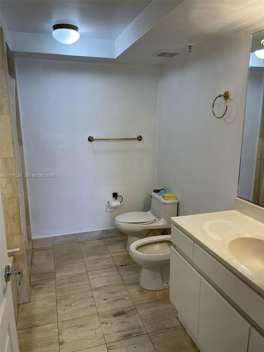 Bathroom featuring a white vanity with an integrated sink, natural stone-finish floor tiling, wall-mounted metallic fixtures, and a glass mirror