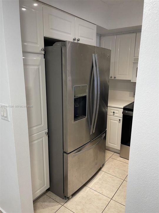 Kitchen featuring white shaker-style cabinetry, stainless steel French-door refrigerator with external water dispenser, and tiled flooring