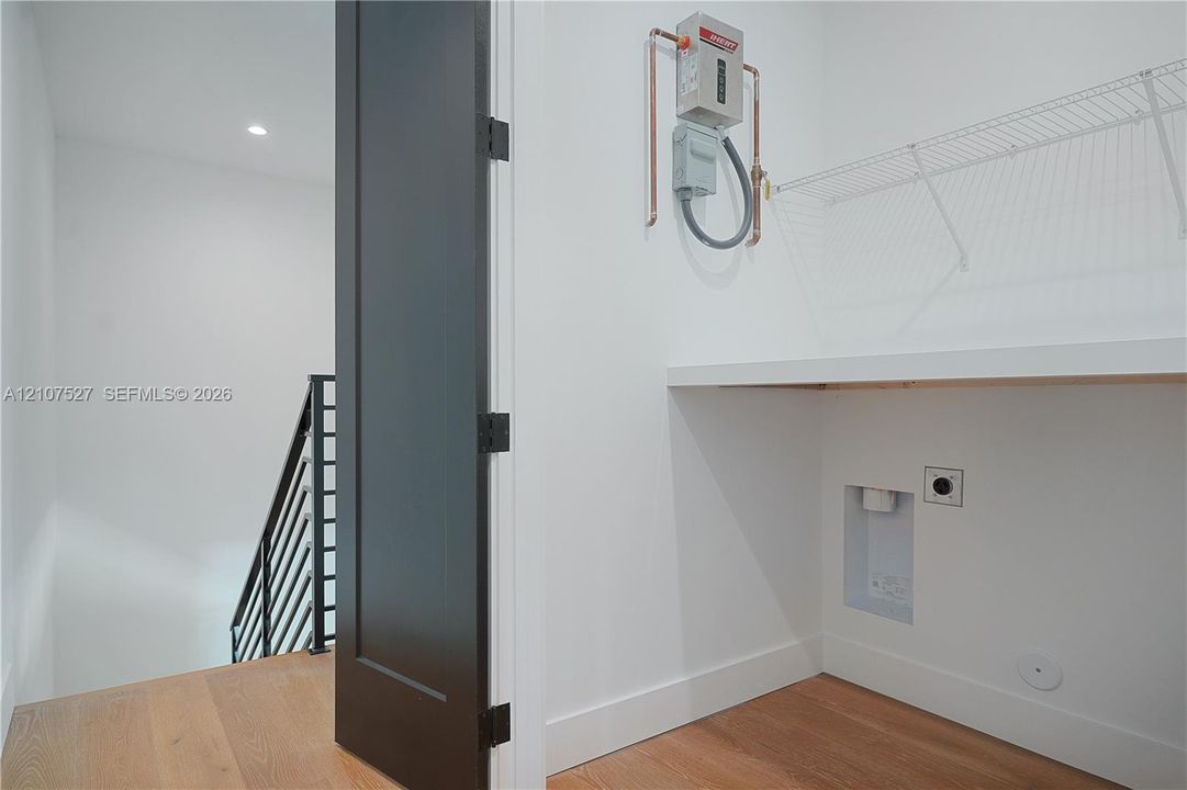 Utility space featuring wood-finish flooring, a wall-mounted tankless water heater, built-in shelving, and a solid-core dark finish interior door