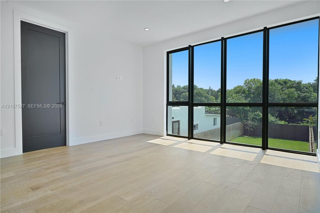 Floor-to-ceiling windows with black frames, wood-finish flooring, and a solid-core interior door with matte black hardware
