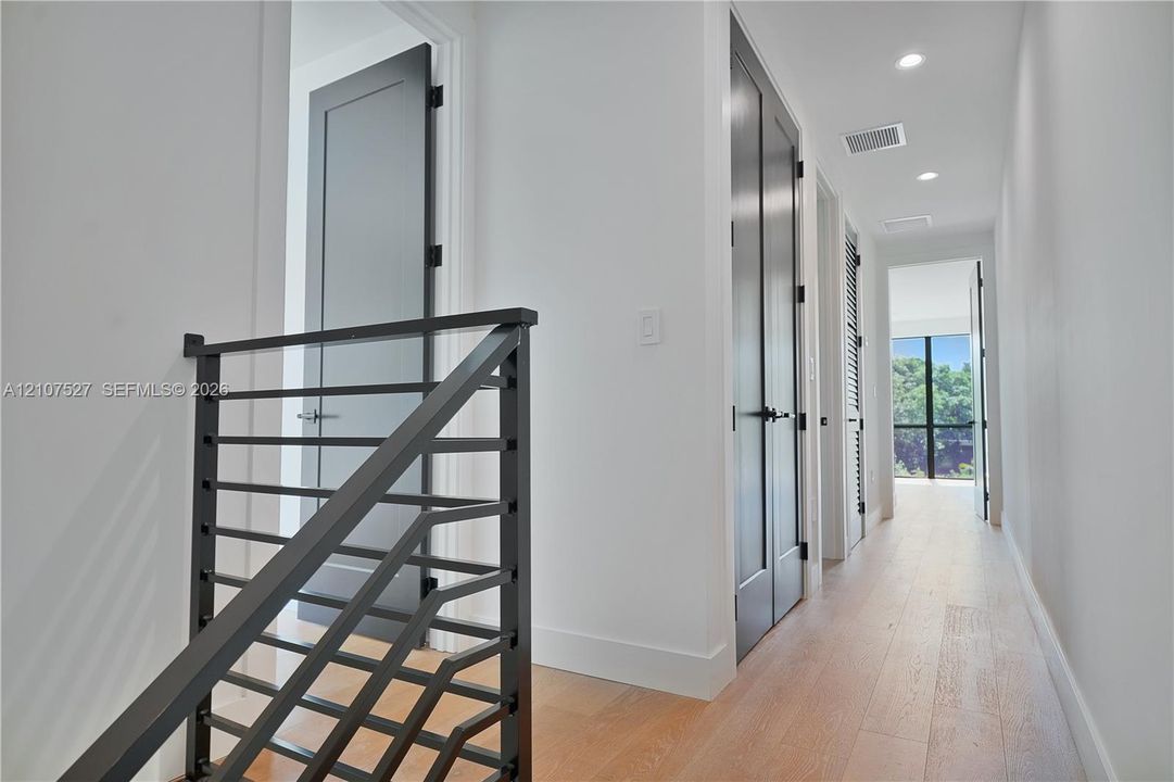 Hallway featuring wood-finish flooring, recessed lighting, matte black metal railing, and high-contrast dark-toned doors