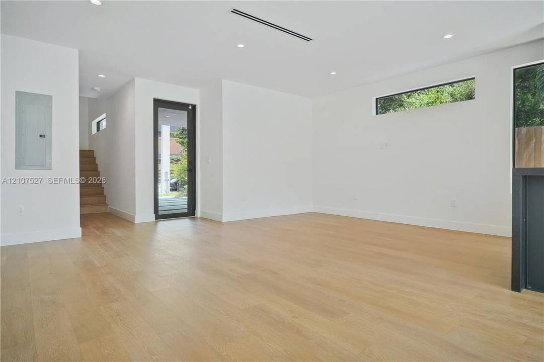 Open-concept interior featuring light wood-finish flooring, recessed lighting, clerestory windows, and a glass-paneled exterior door