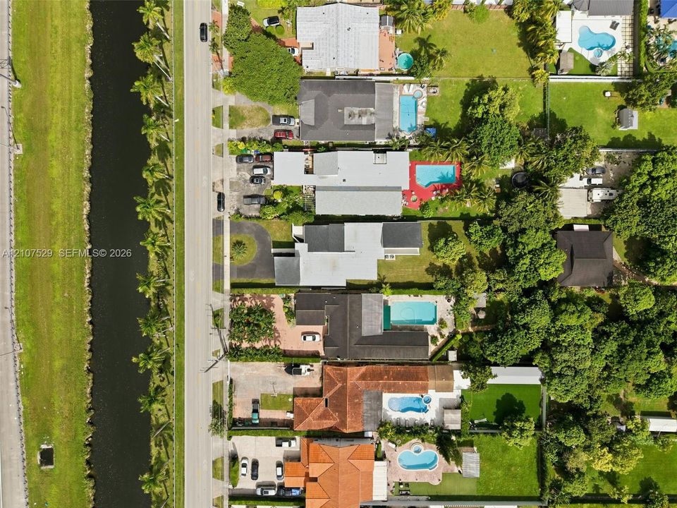 Aerial view of waterfront property featuring a canal-side location, private swimming pool, and paved driveway