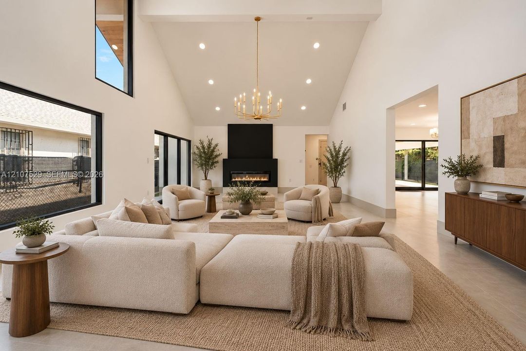 Vaulted ceiling with recessed lighting, floor-to-ceiling black-framed windows, linear fireplace with a matte black surround, and metal multi-tier chandelier