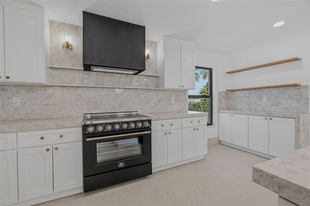 Kitchen featuring shaker-style cabinetry, stone countertops with matching backsplash, a large center island, built-in beverage refrigerator, and recessed lighting